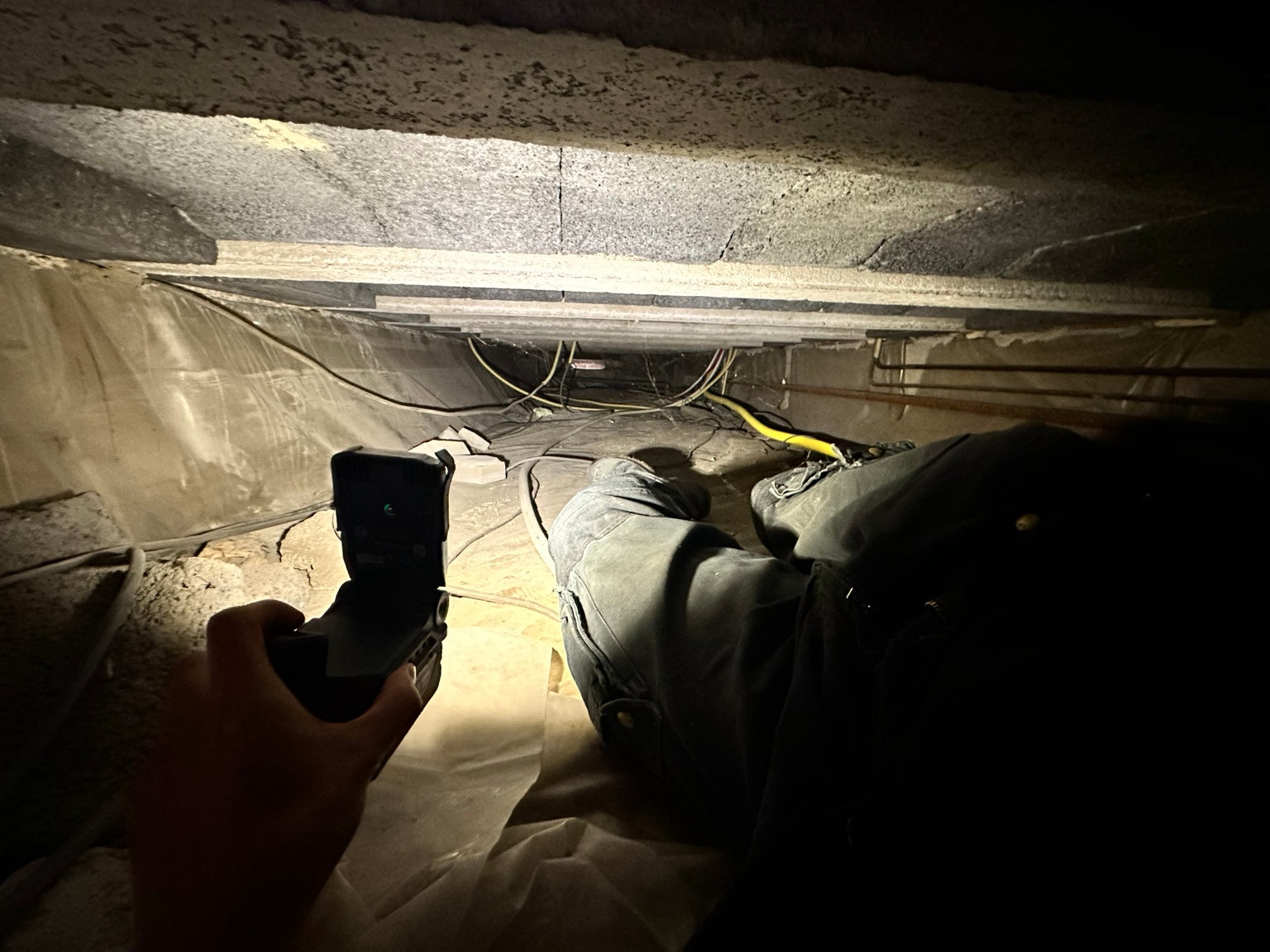 Inspectie van een kruipruimte met leidingen en vloerconstructie